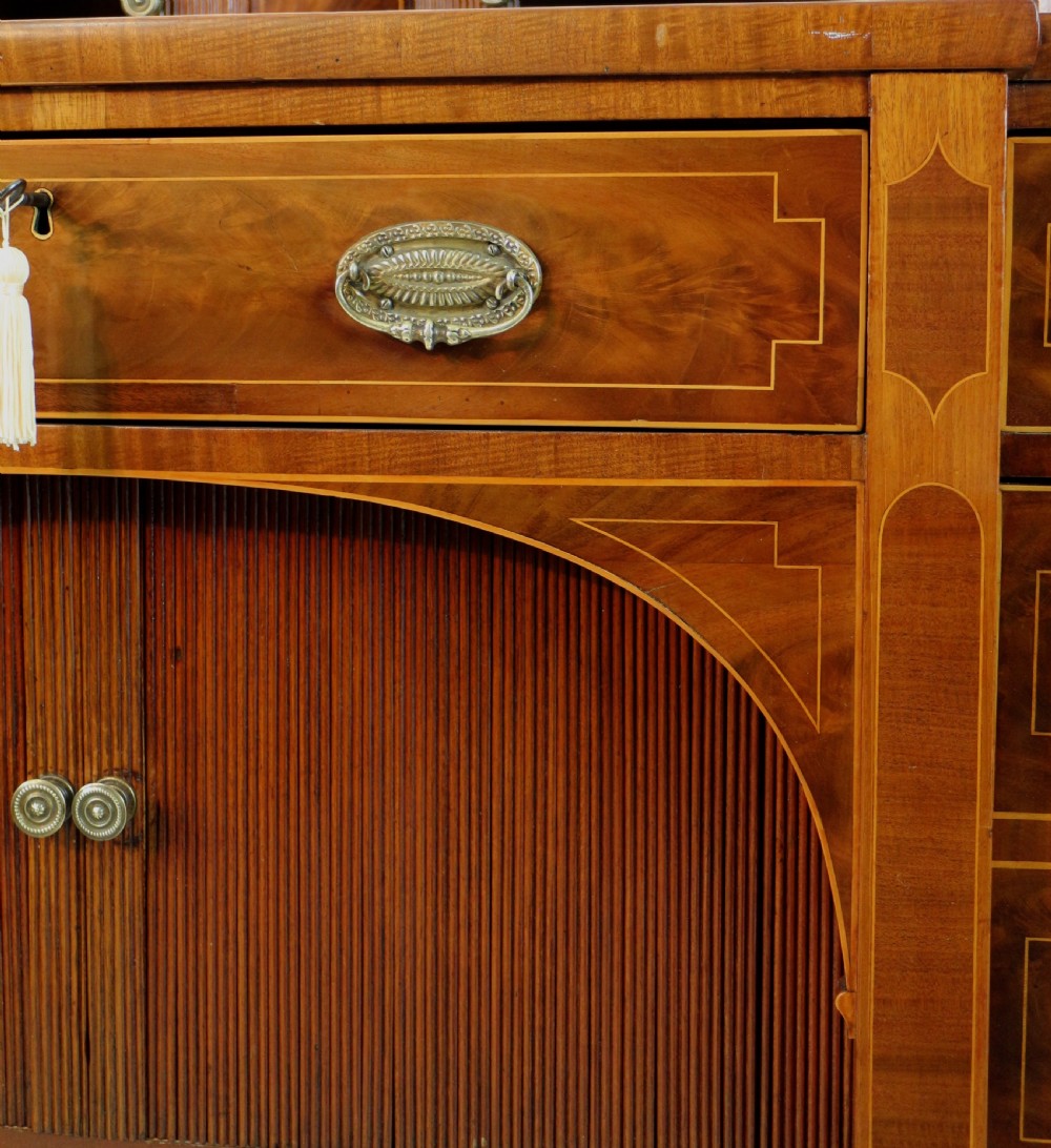 A George III Scottish flame mahogany stage-back sideboard featuring curved side drawers, inlay details, central tambour cupboards, and slender turned legs. View XII
