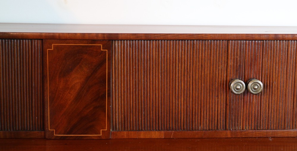 A George III Scottish flame mahogany stage-back sideboard featuring curved side drawers, inlay details, central tambour cupboards, and slender turned legs. View XIII