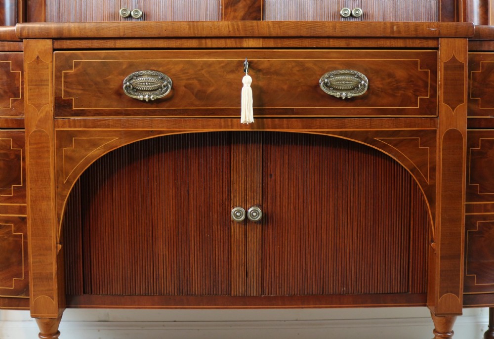 A George III Scottish flame mahogany stage-back sideboard featuring curved side drawers, inlay details, central tambour cupboards, and slender turned legs. View XIV