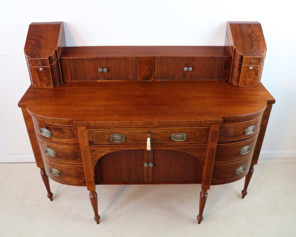 A George III Scottish flame mahogany stage-back sideboard featuring curved side drawers, inlay details, central tambour cupboards, and slender turned legs. View XV