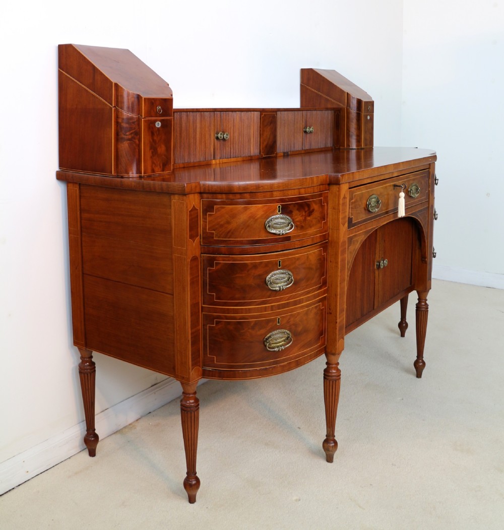 A George III Scottish flame mahogany stage-back sideboard featuring curved side drawers, inlay details, central tambour cupboards, and slender turned legs. View XVIII
