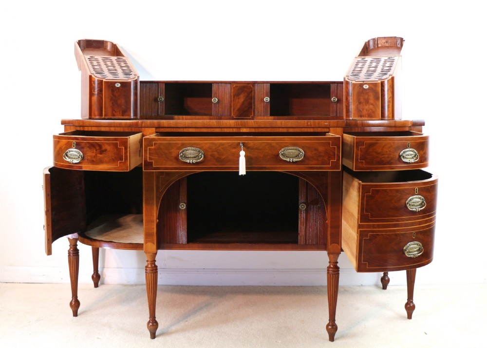 A George III Scottish flame mahogany stage-back sideboard featuring curved side drawers, inlay details, central tambour cupboards, and slender turned legs. View XIX