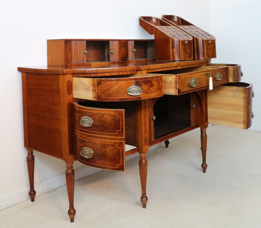 A George III Scottish flame mahogany stage-back sideboard featuring curved side drawers, inlay details, central tambour cupboards, and slender turned legs. View XX