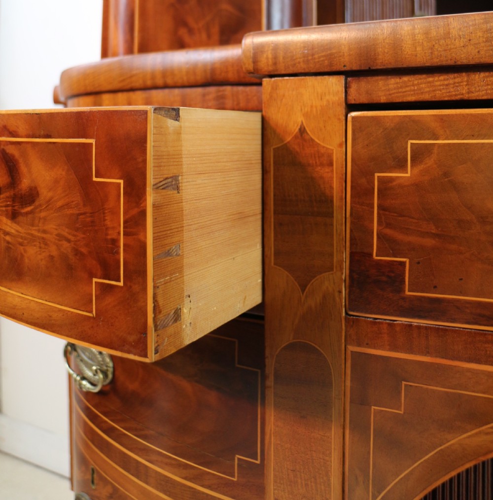 A George III Scottish flame mahogany stage-back sideboard featuring curved side drawers, inlay details, central tambour cupboards, and slender turned legs. View XXI