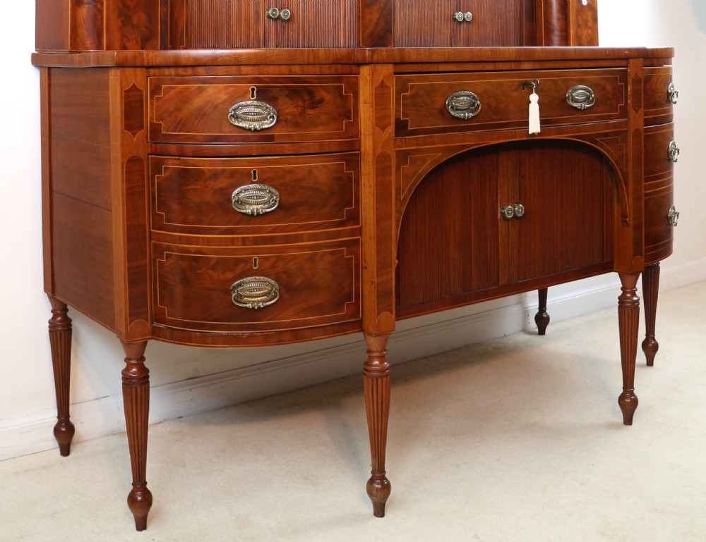 A George III Scottish flame mahogany stage-back sideboard featuring curved side drawers, inlay details, central tambour cupboards, and slender turned legs. View XXII