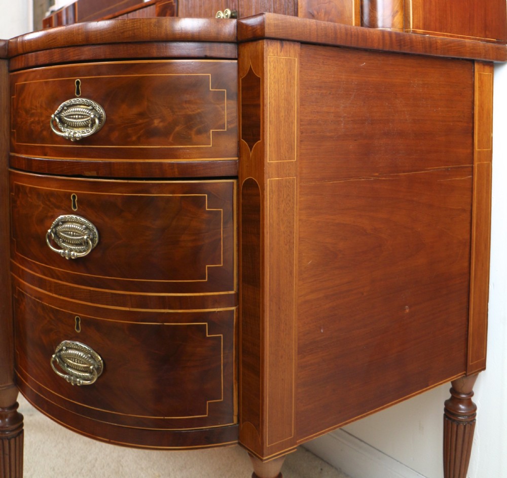 A George III Scottish flame mahogany stage-back sideboard featuring curved side drawers, inlay details, central tambour cupboards, and slender turned legs. View XXIV