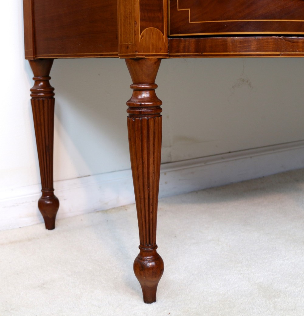 A George III Scottish flame mahogany stage-back sideboard featuring curved side drawers, inlay details, central tambour cupboards, and slender turned legs. View XXV