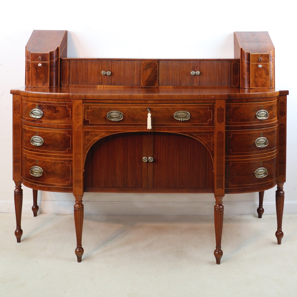 A George III Scottish flame mahogany stage-back sideboard featuring curved side drawers, inlay details, central tambour cupboards, and slender turned legs.