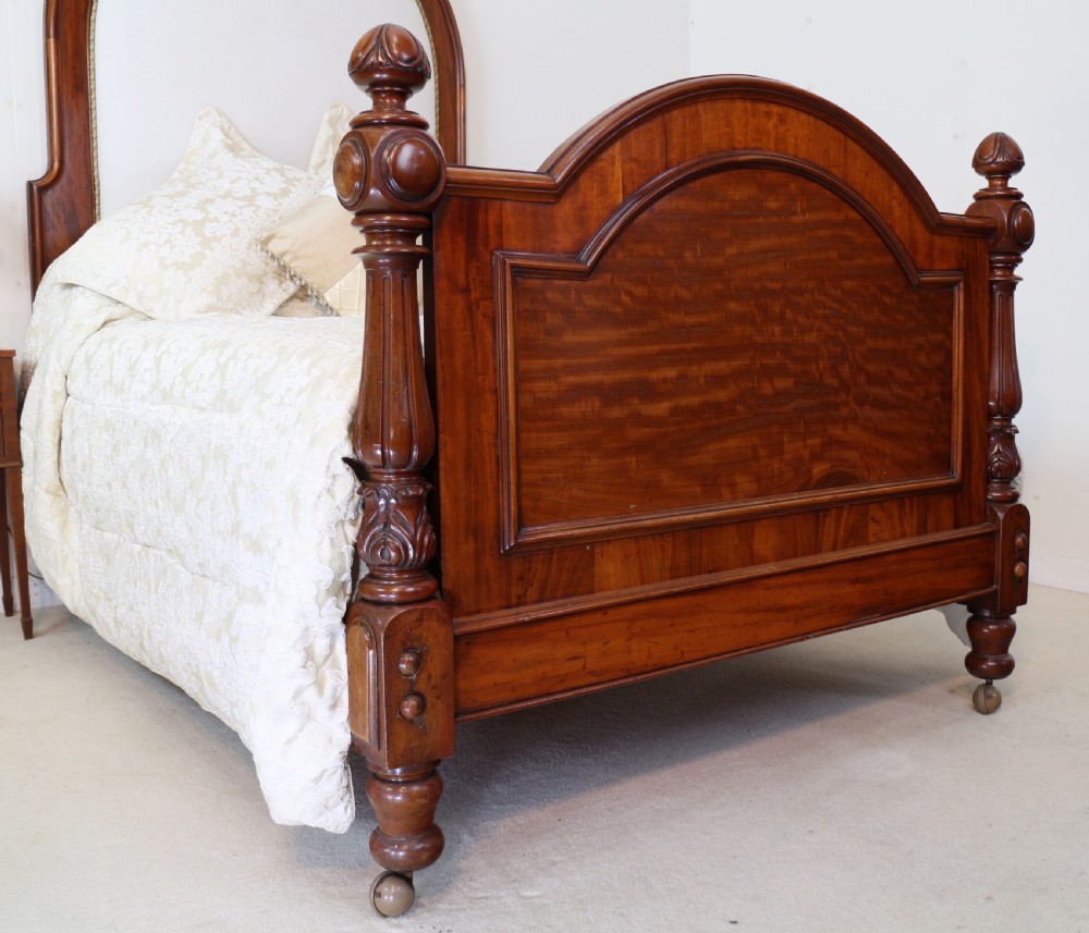 A Victorian mahogany double bed featuring a high arched upholstered headboard, a flame mahogany footboard with carved posts, and brass castors. View II
