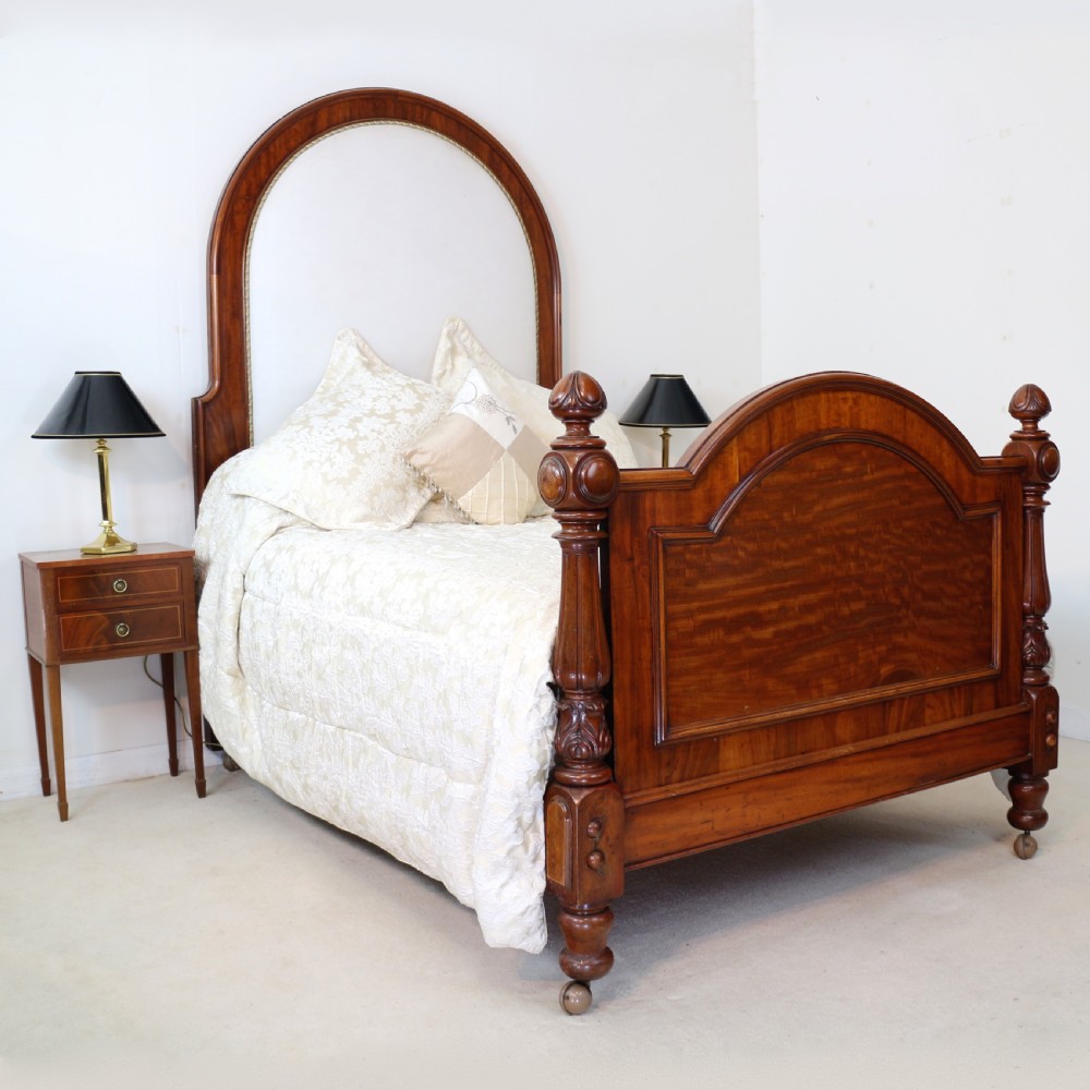 A Victorian mahogany double bed featuring a high arched upholstered headboard, a flame mahogany footboard with carved posts, and brass castors. View III