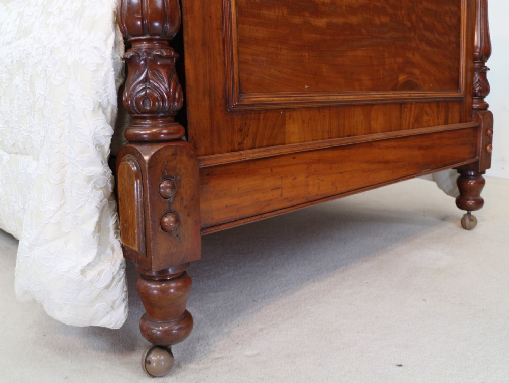 A Victorian mahogany double bed featuring a high arched upholstered headboard, a flame mahogany footboard with carved posts, and brass castors. View XI