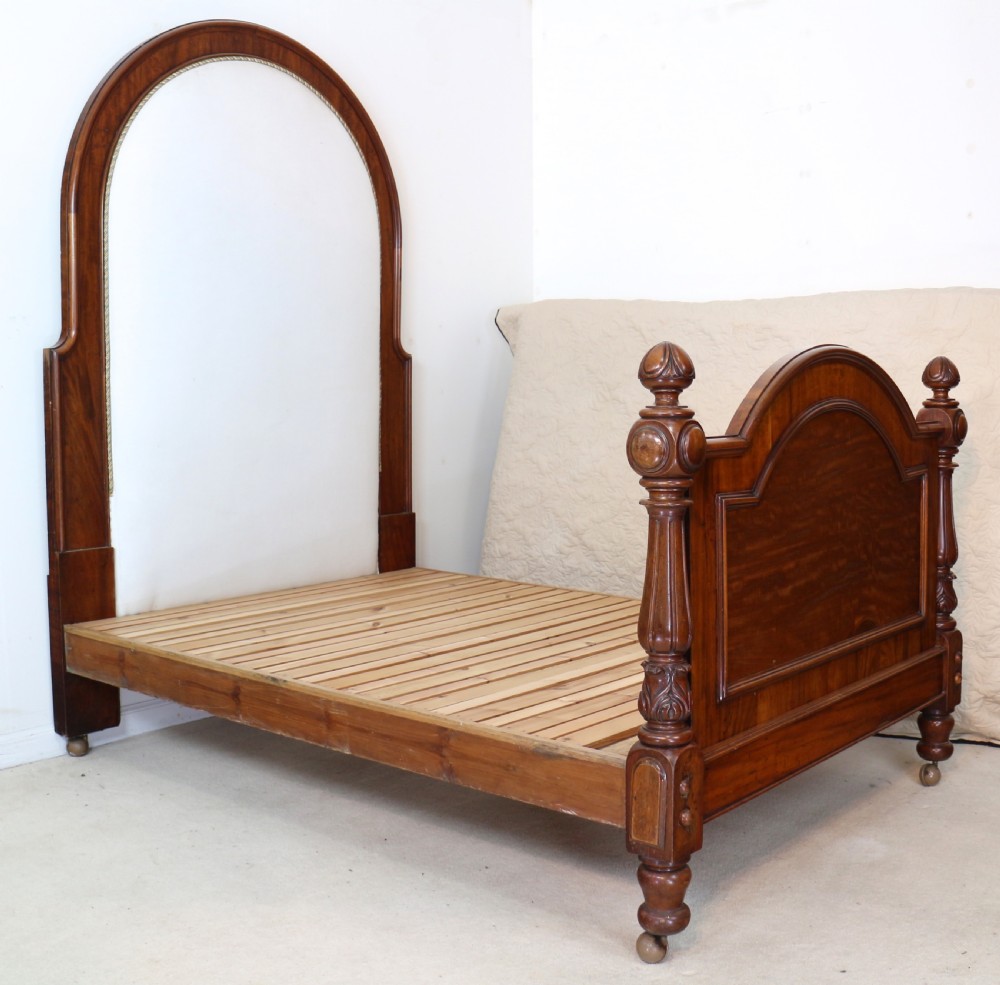 A Victorian mahogany double bed featuring a high arched upholstered headboard, a flame mahogany footboard with carved posts, and brass castors. View XVI