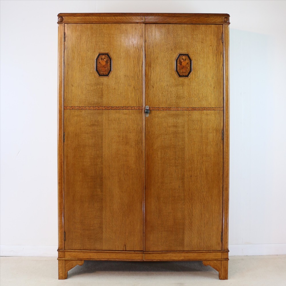 A three-piece golden oak Art Deco bedroom suite featuring a double wardrobe, dressing table with an arched mirror, and a small cupboard chest, all decorated with marquetry medallions. View II