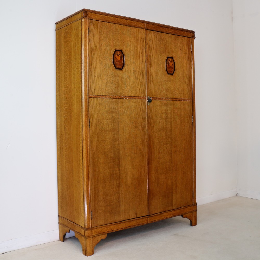 A three-piece golden oak Art Deco bedroom suite featuring a double wardrobe, dressing table with an arched mirror, and a small cupboard chest, all decorated with marquetry medallions. View III
