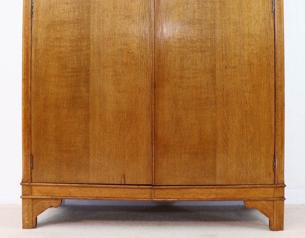 A three-piece golden oak Art Deco bedroom suite featuring a double wardrobe, dressing table with an arched mirror, and a small cupboard chest, all decorated with marquetry medallions. View VI