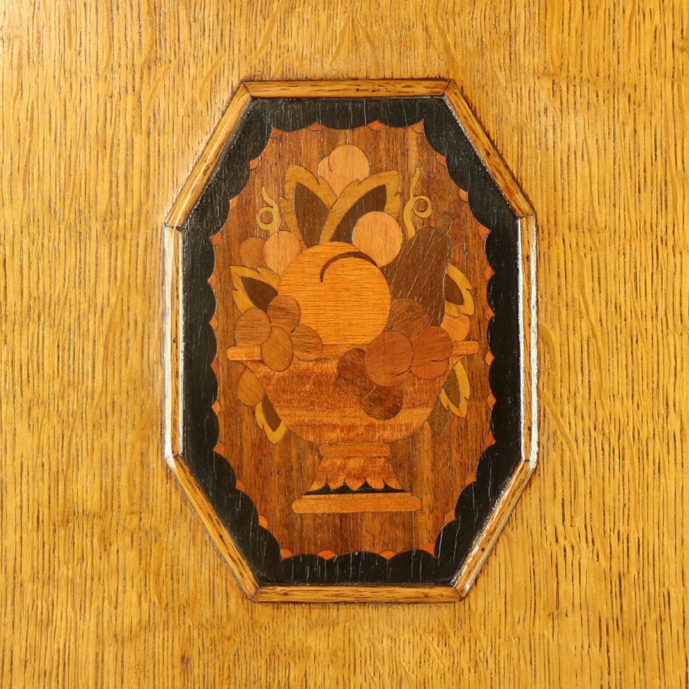 A three-piece golden oak Art Deco bedroom suite featuring a double wardrobe, dressing table with an arched mirror, and a small cupboard chest, all decorated with marquetry medallions. View VII