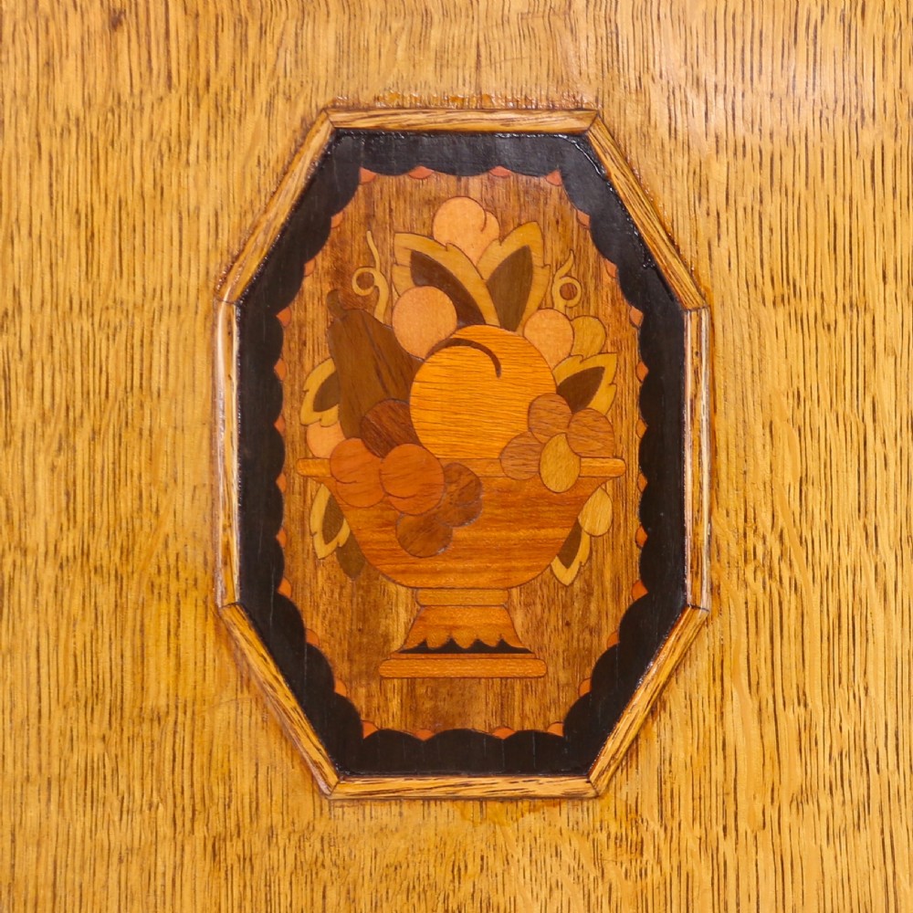 A three-piece golden oak Art Deco bedroom suite featuring a double wardrobe, dressing table with an arched mirror, and a small cupboard chest, all decorated with marquetry medallions. View VIII
