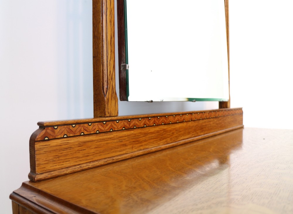 A three-piece golden oak Art Deco bedroom suite featuring a double wardrobe, dressing table with an arched mirror, and a small cupboard chest, all decorated with marquetry medallions. View XVI