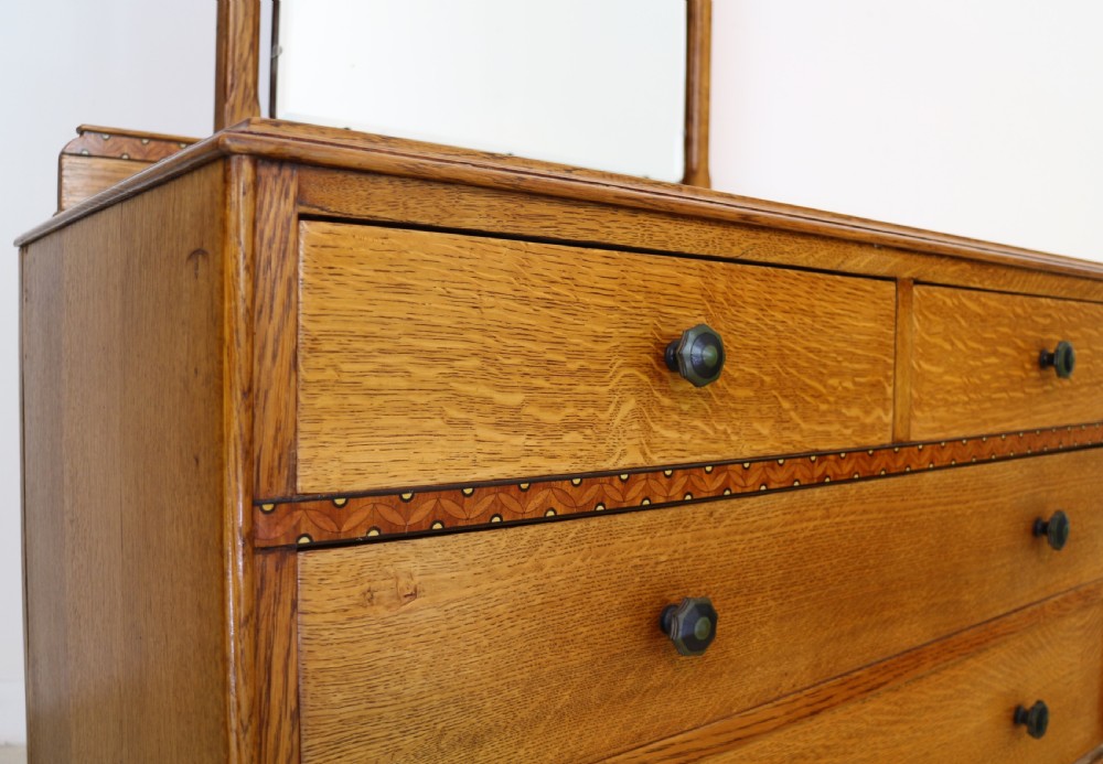 A three-piece golden oak Art Deco bedroom suite featuring a double wardrobe, dressing table with an arched mirror, and a small cupboard chest, all decorated with marquetry medallions. View XVII