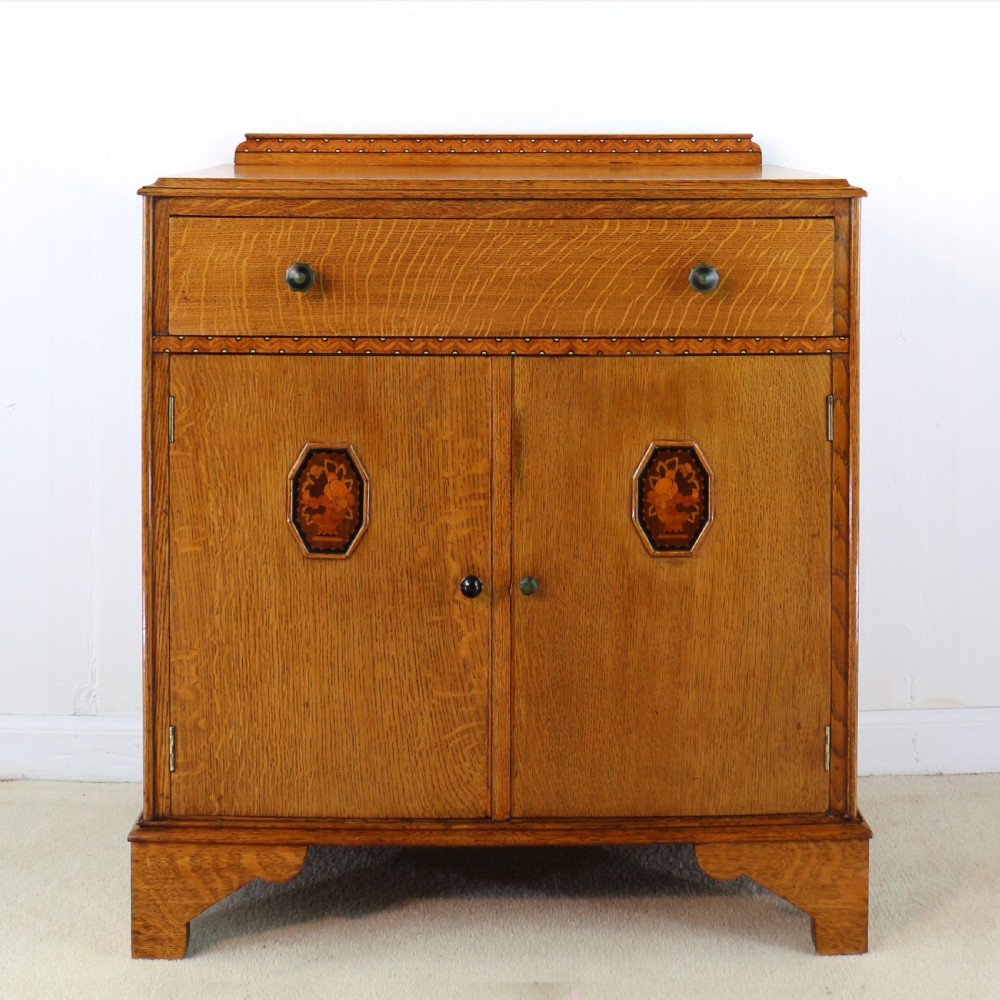 A three-piece golden oak Art Deco bedroom suite featuring a double wardrobe, dressing table with an arched mirror, and a small cupboard chest, all decorated with marquetry medallions. View XIX
