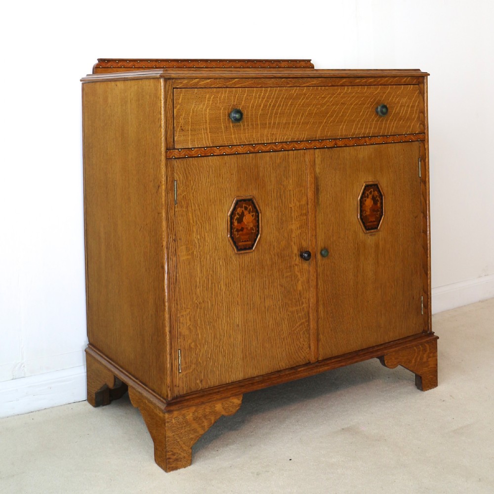 A three-piece golden oak Art Deco bedroom suite featuring a double wardrobe, dressing table with an arched mirror, and a small cupboard chest, all decorated with marquetry medallions. View XX