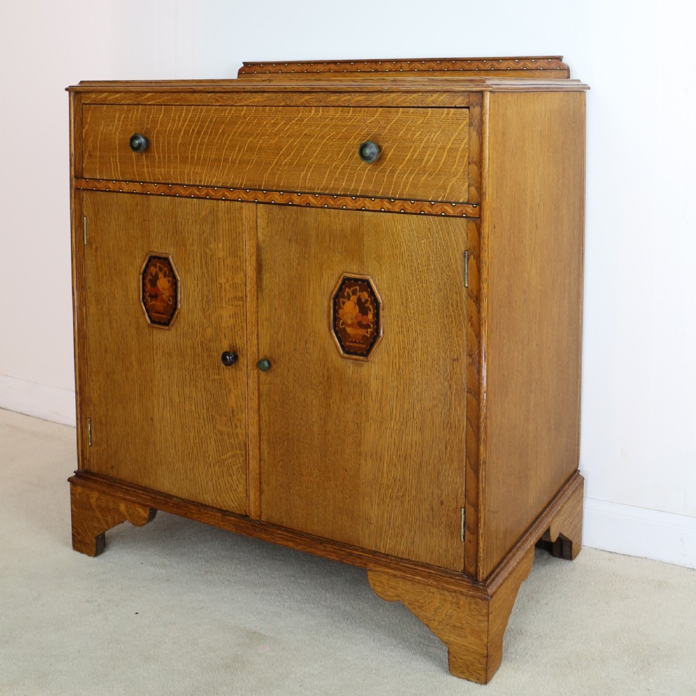 A three-piece golden oak Art Deco bedroom suite featuring a double wardrobe, dressing table with an arched mirror, and a small cupboard chest, all decorated with marquetry medallions. View XXI