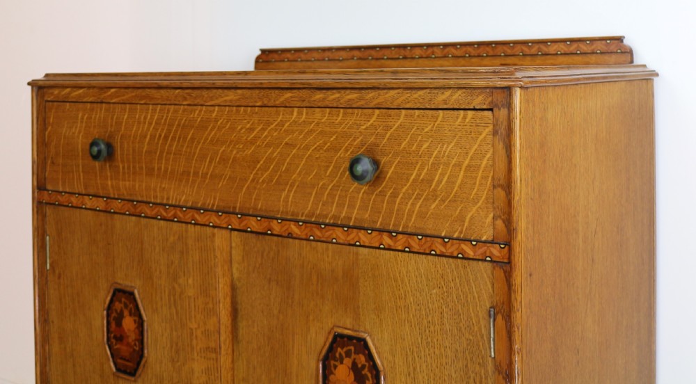 A three-piece golden oak Art Deco bedroom suite featuring a double wardrobe, dressing table with an arched mirror, and a small cupboard chest, all decorated with marquetry medallions. View XXII