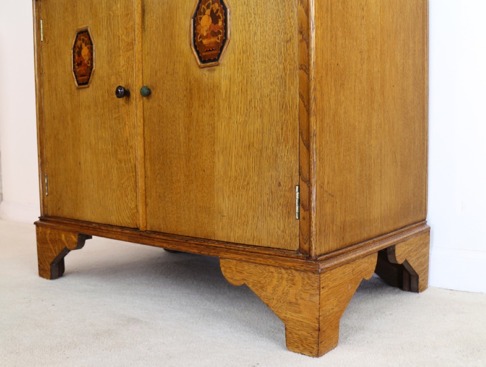 A three-piece golden oak Art Deco bedroom suite featuring a double wardrobe, dressing table with an arched mirror, and a small cupboard chest, all decorated with marquetry medallions. View XXIII