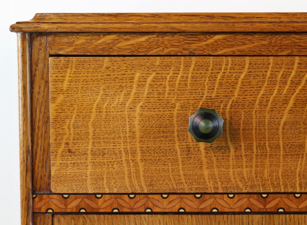 A three-piece golden oak Art Deco bedroom suite featuring a double wardrobe, dressing table with an arched mirror, and a small cupboard chest, all decorated with marquetry medallions. View XXIV