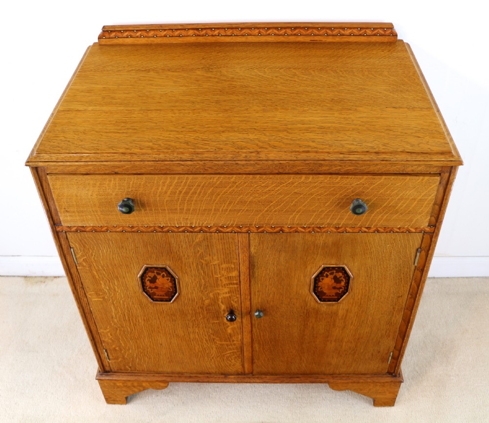 A three-piece golden oak Art Deco bedroom suite featuring a double wardrobe, dressing table with an arched mirror, and a small cupboard chest, all decorated with marquetry medallions. View XXVI