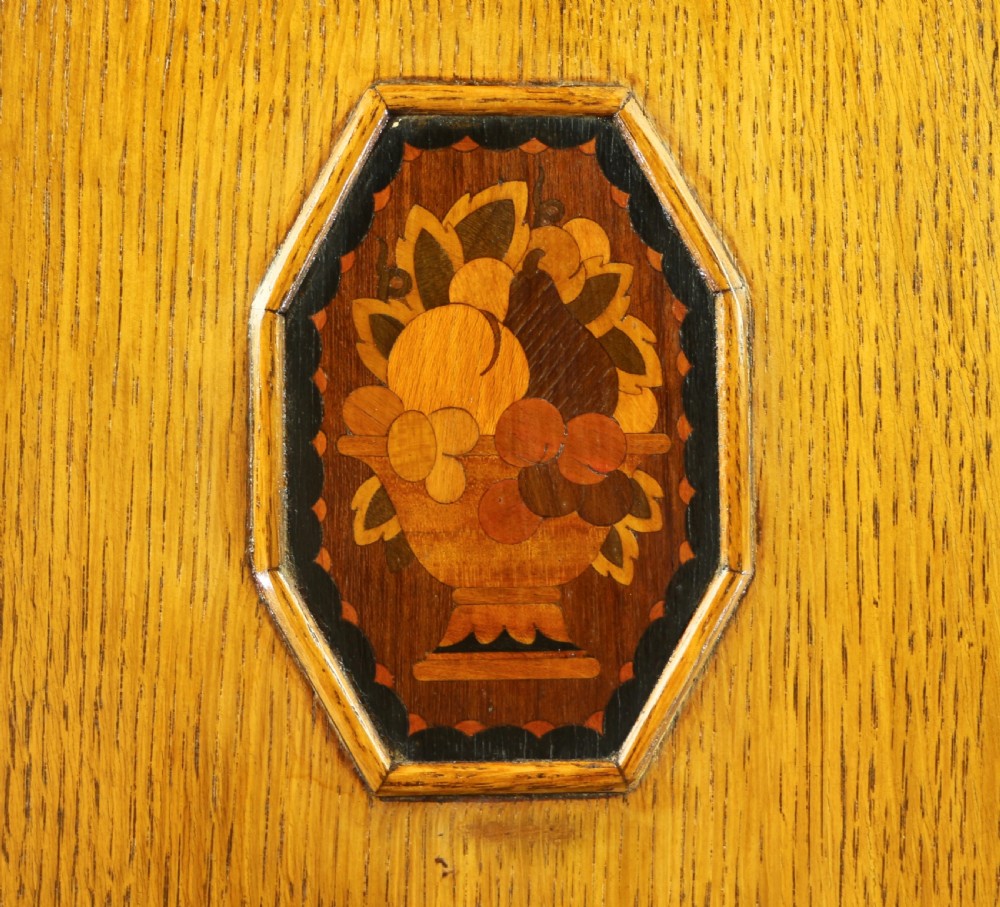 A three-piece golden oak Art Deco bedroom suite featuring a double wardrobe, dressing table with an arched mirror, and a small cupboard chest, all decorated with marquetry medallions. View XXVII