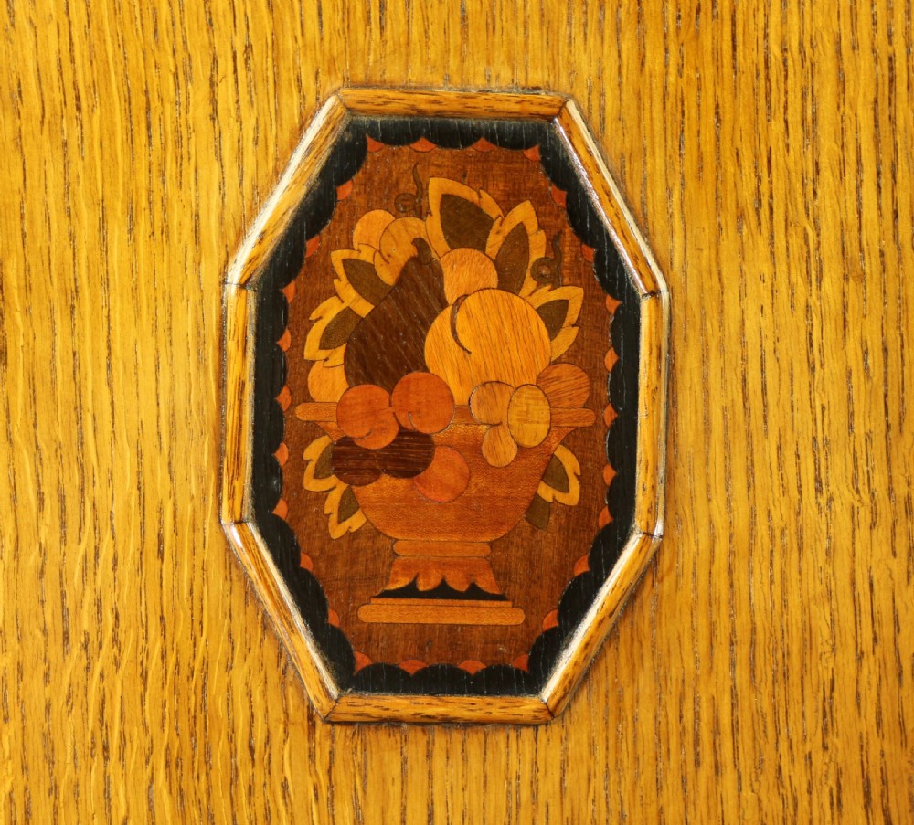 A three-piece golden oak Art Deco bedroom suite featuring a double wardrobe, dressing table with an arched mirror, and a small cupboard chest, all decorated with marquetry medallions. View XXVIII