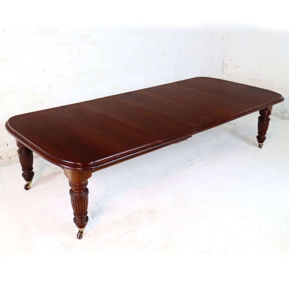 A large Victorian mahogany extending dining table with rounded corners, three insertion leaves, and carved fluted turned legs resting on brass castors.