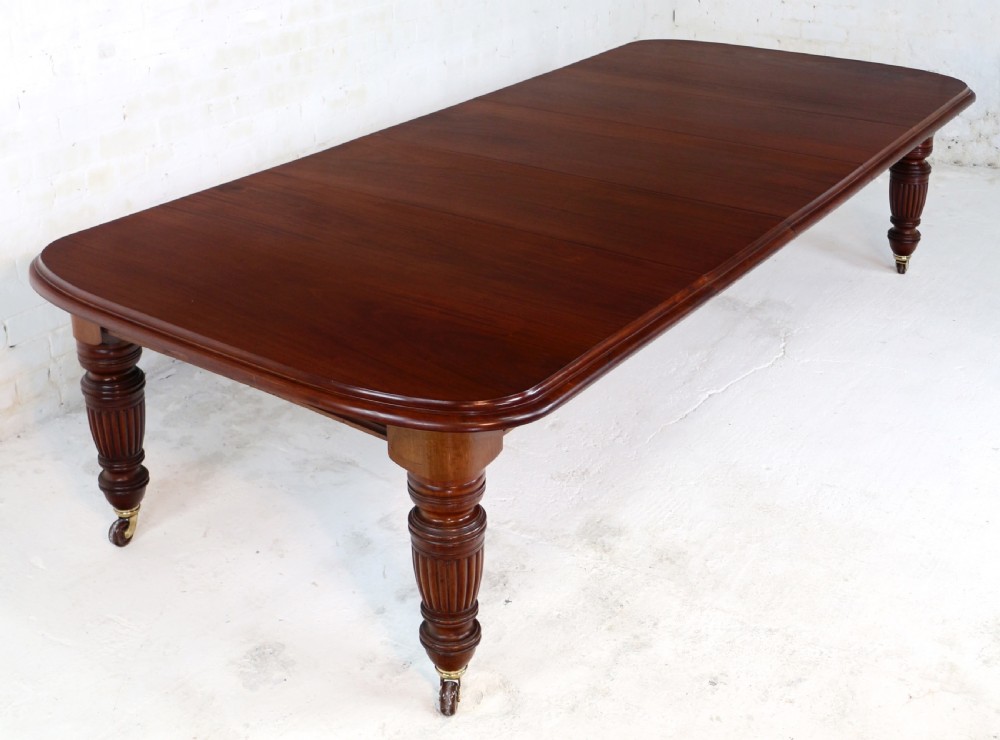 A large Victorian mahogany extending dining table with rounded corners, three insertion leaves, and carved fluted turned legs resting on brass castors. View II