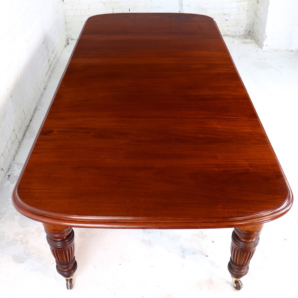 A large Victorian mahogany extending dining table with rounded corners, three insertion leaves, and carved fluted turned legs resting on brass castors. View III
