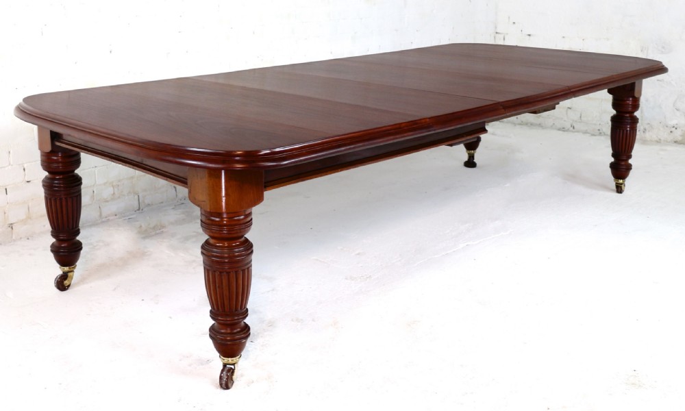 A large Victorian mahogany extending dining table with rounded corners, three insertion leaves, and carved fluted turned legs resting on brass castors. View V