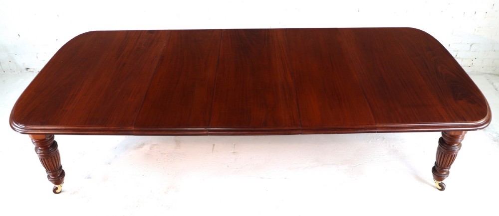 A large Victorian mahogany extending dining table with rounded corners, three insertion leaves, and carved fluted turned legs resting on brass castors. View VI