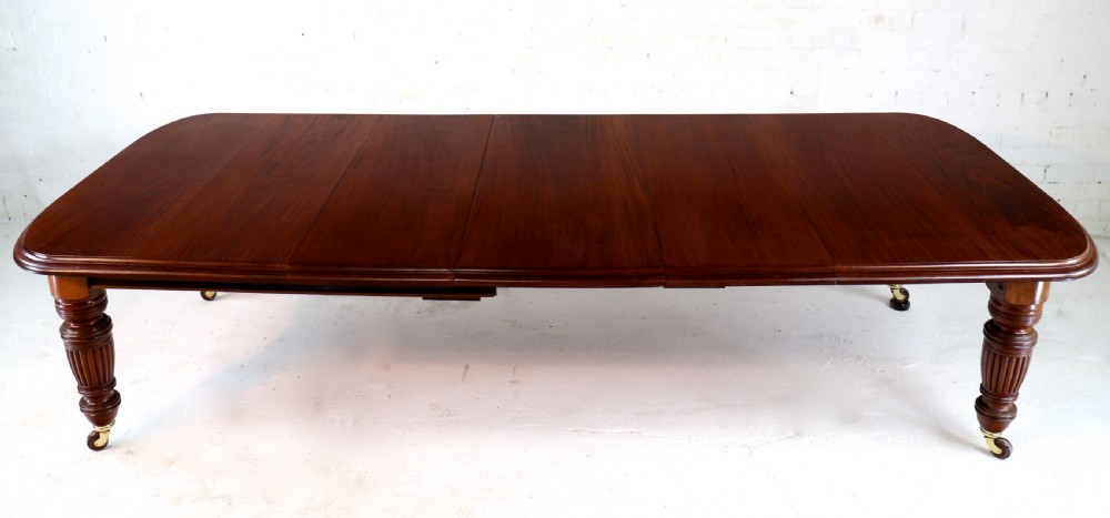A large Victorian mahogany extending dining table with rounded corners, three insertion leaves, and carved fluted turned legs resting on brass castors. View VII