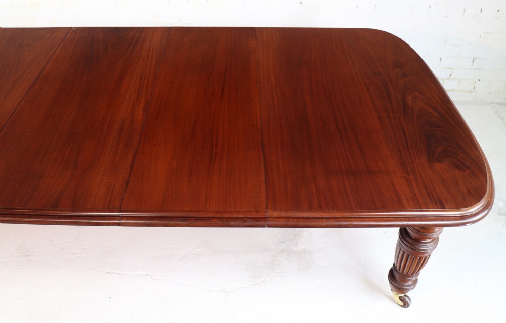 A large Victorian mahogany extending dining table with rounded corners, three insertion leaves, and carved fluted turned legs resting on brass castors. View VIII