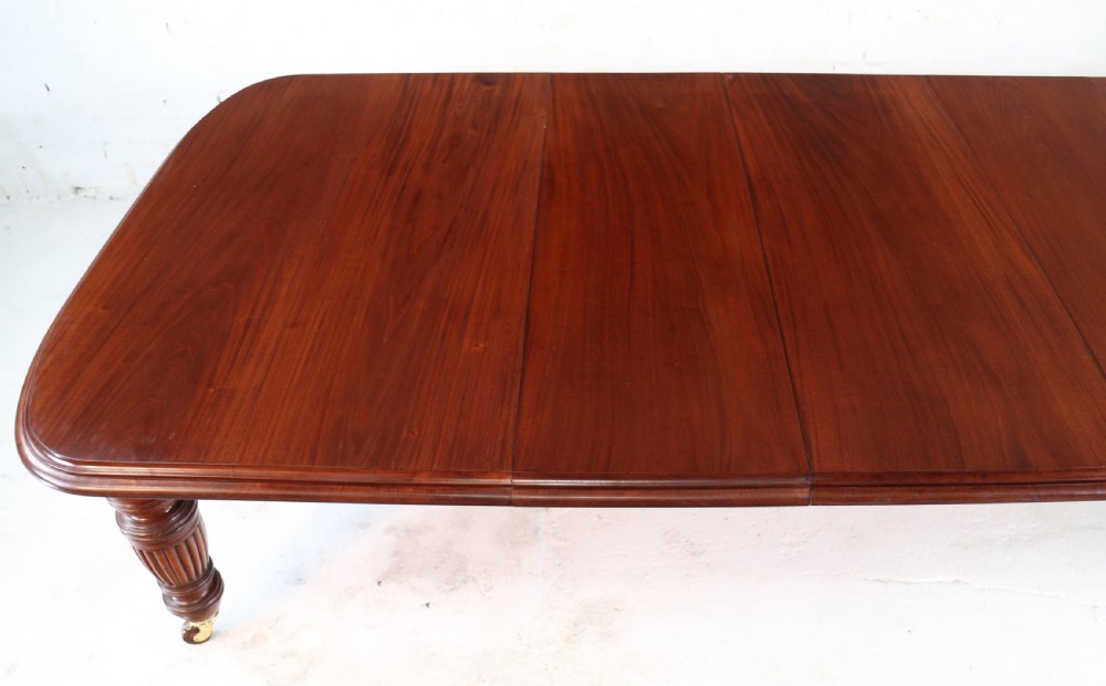 A large Victorian mahogany extending dining table with rounded corners, three insertion leaves, and carved fluted turned legs resting on brass castors. View IX