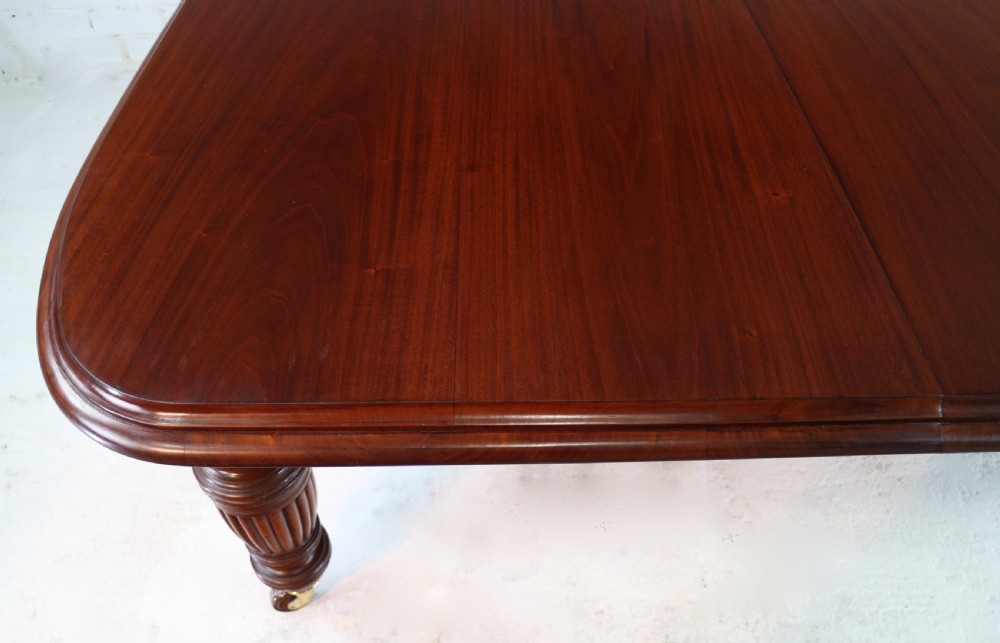 A large Victorian mahogany extending dining table with rounded corners, three insertion leaves, and carved fluted turned legs resting on brass castors. View X