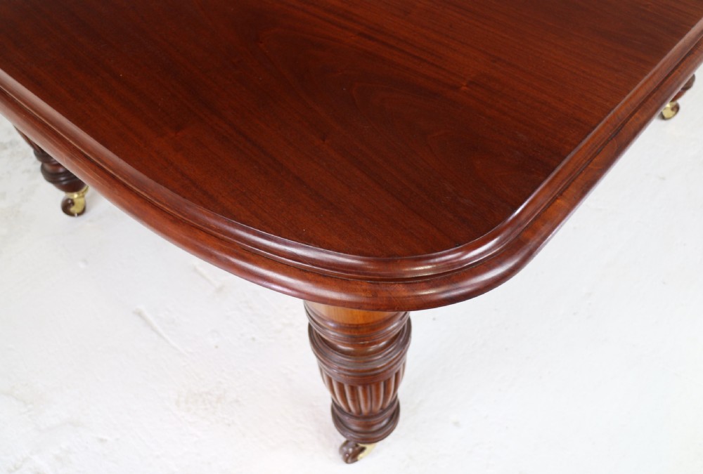 A large Victorian mahogany extending dining table with rounded corners, three insertion leaves, and carved fluted turned legs resting on brass castors. View XI