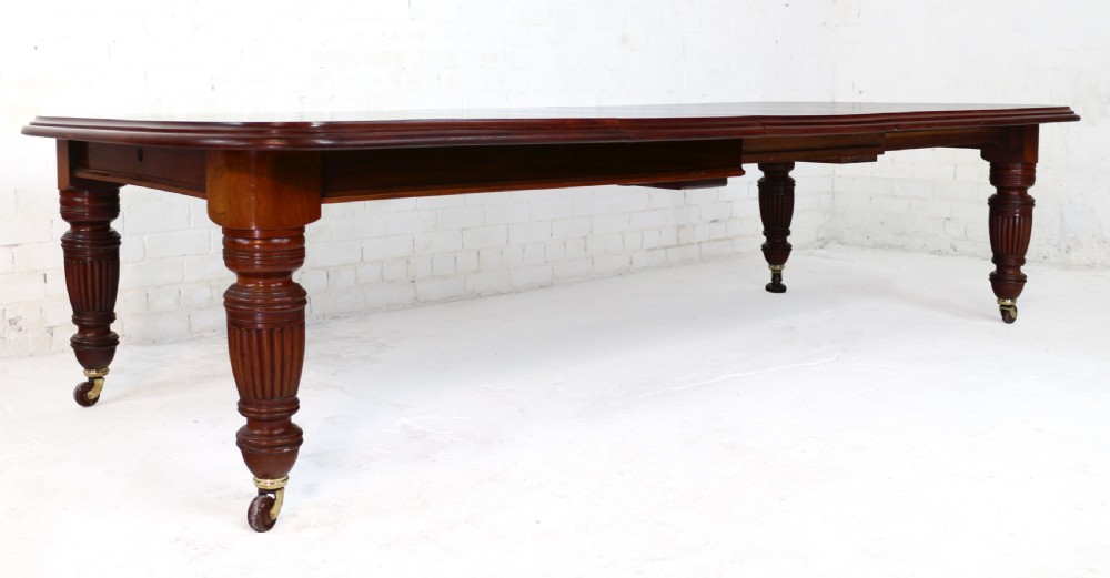 A large Victorian mahogany extending dining table with rounded corners, three insertion leaves, and carved fluted turned legs resting on brass castors. View XII