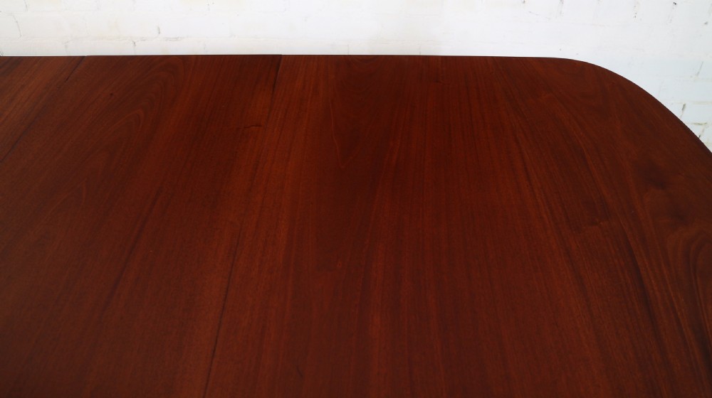 A large Victorian mahogany extending dining table with rounded corners, three insertion leaves, and carved fluted turned legs resting on brass castors. View XIII