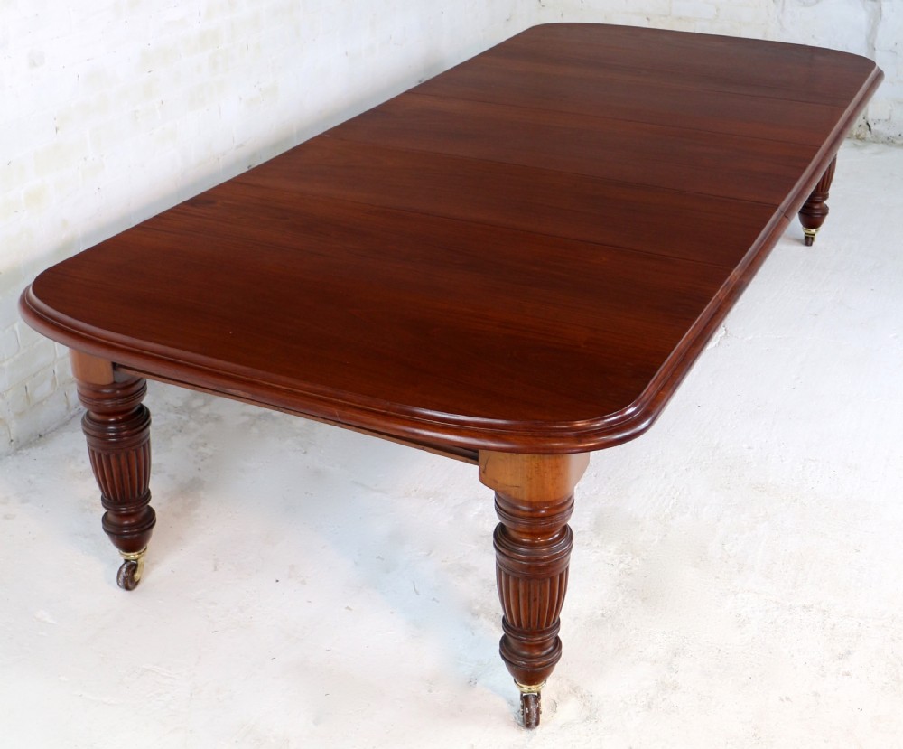 A large Victorian mahogany extending dining table with rounded corners, three insertion leaves, and carved fluted turned legs resting on brass castors. View XIV