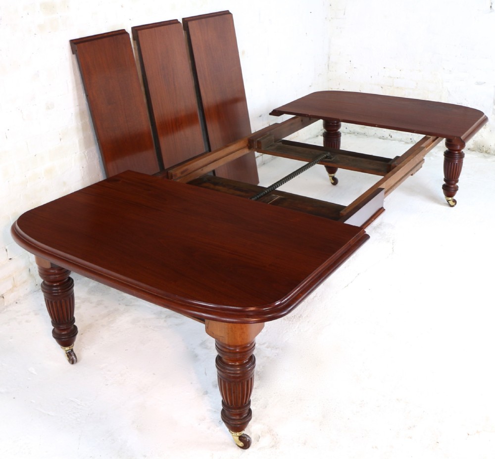 A large Victorian mahogany extending dining table with rounded corners, three insertion leaves, and carved fluted turned legs resting on brass castors. View XV
