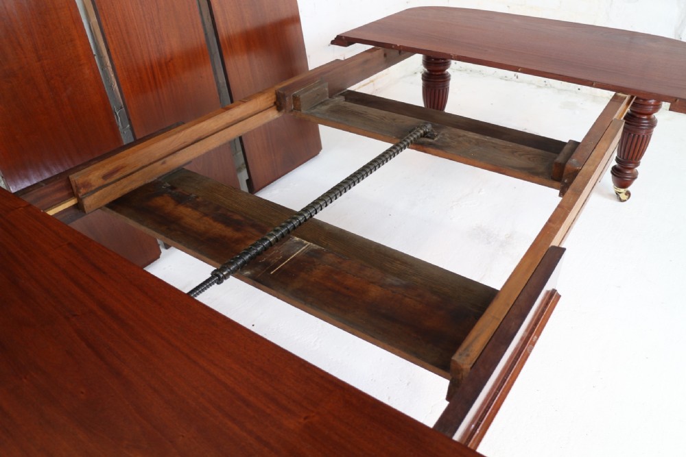 A large Victorian mahogany extending dining table with rounded corners, three insertion leaves, and carved fluted turned legs resting on brass castors. View XVI