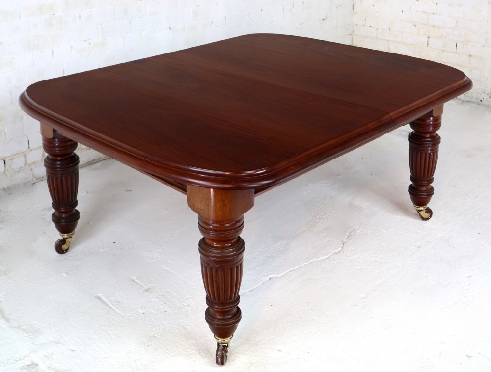 A large Victorian mahogany extending dining table with rounded corners, three insertion leaves, and carved fluted turned legs resting on brass castors. View XVII