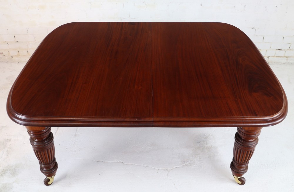 A large Victorian mahogany extending dining table with rounded corners, three insertion leaves, and carved fluted turned legs resting on brass castors. View XVIII