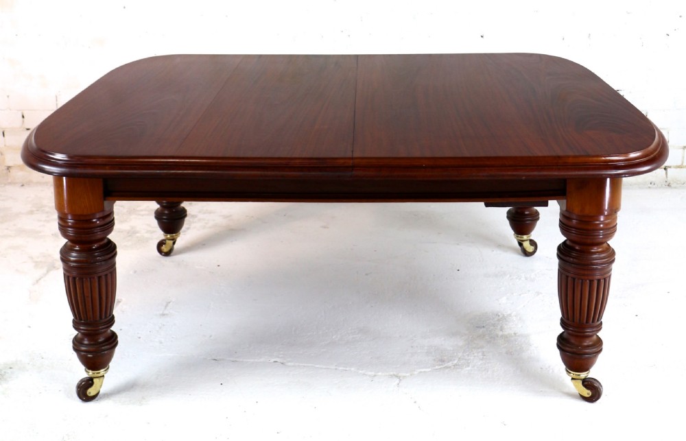 A large Victorian mahogany extending dining table with rounded corners, three insertion leaves, and carved fluted turned legs resting on brass castors. View XIX